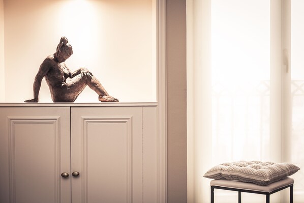 A statue of a seated figure on a cabinet, a cushioned bench, and a window with curtains. - UNIQUE Paseo de Gracia CASA BATLLÓ Barcelona Center (Barcelona)