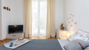 Un dormitorio moderno con cama, mesita de noche, televisor y cortinas.