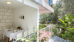 Un comedor con una mesa lista para cuatro personas, una pared blanca y vistas a un jardín con barandilla de metal.