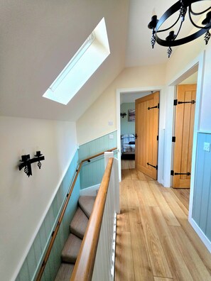 Un escalier avec une rampe en bois, une lucarne et un lustre.