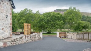 Un bâtiment en pierre doté d’un portail en bois et d’une allée pavée menant à une zone boisée.