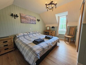 A bedroom with a bed, bedside tables, a desk, a chair, a window, and a chandelier.