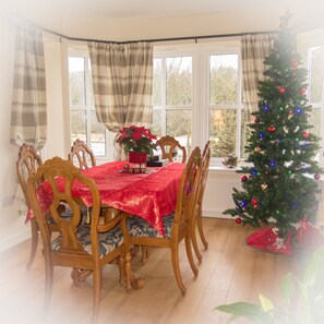 A dining room with a red tablecloth, wooden chairs, a Christmas tree, and a window with curtains.