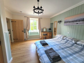 A bedroom with a bed, a desk, a chair, a window with curtains, a chandelier, and a painting on the wall.