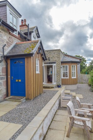 A two-story house with a blue front door, a stone wall, and a wooden porch.