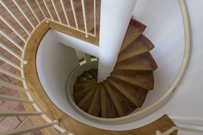 Uma escadaria em espiral com degraus de madeira e guarda-corpos brancos.