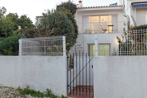 A two-story house with a white exterior, a metal gate, and a staircase leading to the upper floor.