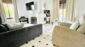 Ett vardagsrum med en grå soffa, en beige soffa, en platt-TV, en takfläkt och ett mönstrat golv.