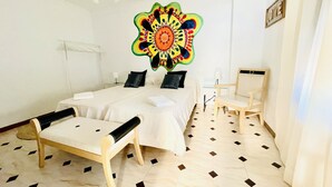 Ett hotellrum med en säng, två stolar, ett litet bord och en dekorativ väggdekoration.