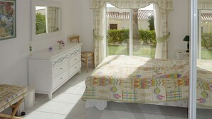 Ein Schlafzimmer mit einem Bett, einem Schminktisch, einem Sessel und einem Fenster mit Blick auf einen Garten.