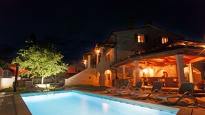 Una piscina amb gandules i una zona de pati coberta, amb parets de pedra i il·luminació càlida.