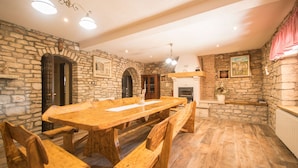 Una àrea de dinar espaiosa amb una taula de fusta gran i bancs, parets de pedra i una llar de foc.
