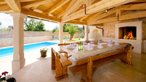 Terrassa exterior amb piscina, bancs de fusta, una llar de pedra i taula de dinar per a sis.