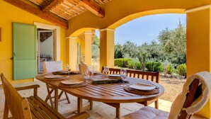 A wooden table set for dining with chairs, a green door, and a view of trees and shrubs. - Large Villa with heated pool and stunning views set among olive trees (Callas)