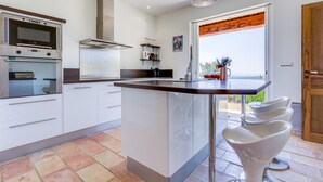 A modern kitchen with a central island, built-in ovens, and a large window with a view. - Large Villa with heated pool and stunning views set among olive trees (Callas)