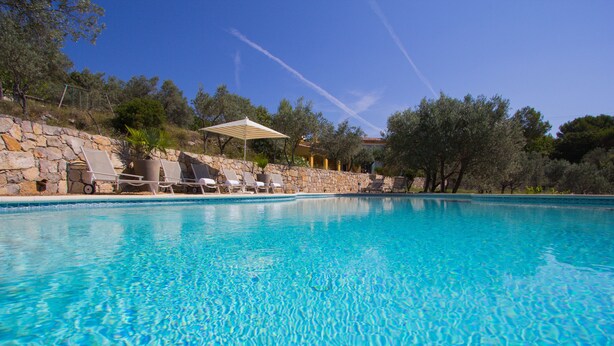 A clear blue swimming pool with lounge chairs and a stone wall. - Large Villa with heated pool and stunning views set among olive trees (Callas)