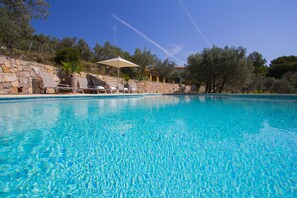 A clear blue swimming pool with lounge chairs and a stone wall. - Large Villa with heated pool and stunning views set among olive trees (Callas)