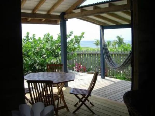 A covered outdoor area with a table and chairs, a hammock, and a view of the ocean.