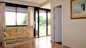 A living room with a sofa, a glass coffee table, and a door leading to an outdoor area.