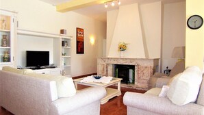 A living room with two sofas, a television, a fireplace, and a clock on the wall.