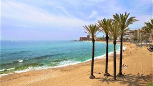 A beach with palm trees, ocean waves, and a distant cityscape.