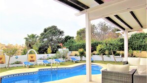 A covered outdoor area with a swimming pool, lounge chairs, and a wicker sofa.