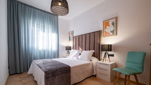 Una habitación de hotel moderna con una cama grande, una mesita de noche con lámpara, una silla y obras de arte en las paredes.