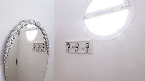 Un baño con un espejo redondo, una lámpara de pared y un perchero con placa de identificación.