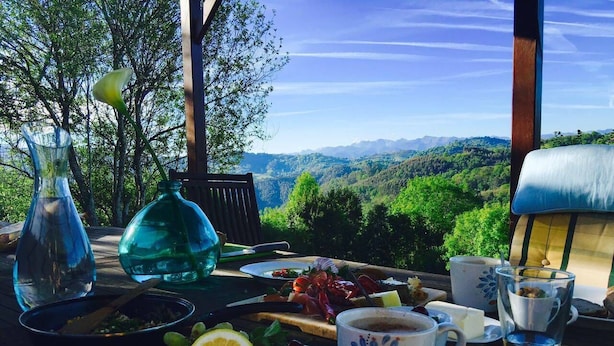 An outdoor dining table with a meal, a view of the mountains, and a wooden structure.