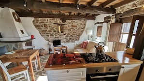 A rustic kitchen with a stone wall, wooden beams, a gas stove, and a built-in oven.