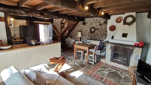 A rustic interior with a stone fireplace, wooden beams, a dining area, and a cozy seating space.