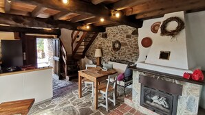 A rustic interior with a stone wall, wooden ceiling beams, a fireplace, and a dining area.