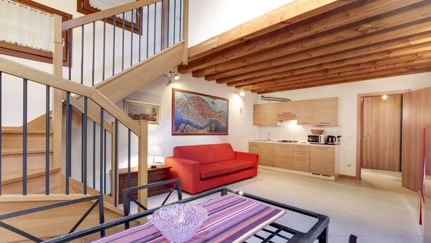 Ein geräumiger Wohnbereich mit einem roten Sofa, einer Holztreppe und einer Küche im Hintergrund.