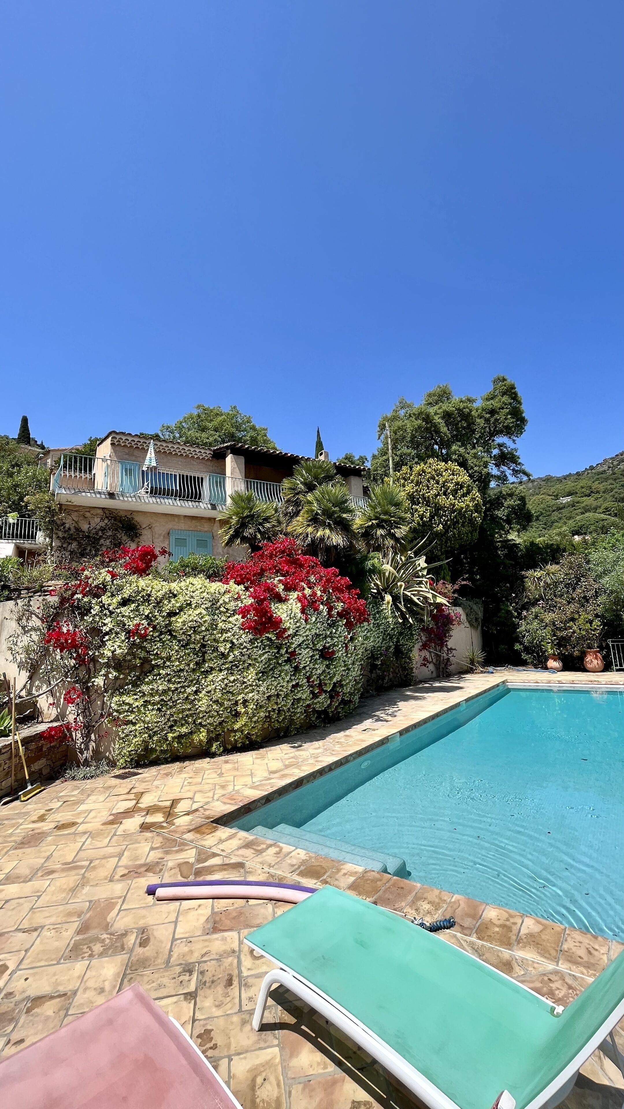A swimming pool with lounge chairs, a stone patio, and a house with a balcony.