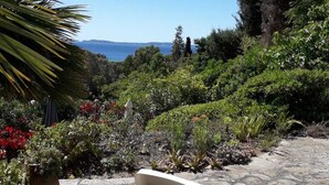 A garden with a stone pathway, a white chair, and a view of the sea. - House / Villa - Le Rayol-Canadel (Rayol-Canadel-Sur-Mer)