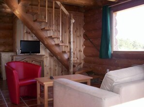 A log cabin interior with a wooden staircase, a television on a wooden table, a red chair, and a white sofa. - Country Cottage / Gite - CHORGES (CHORGES)