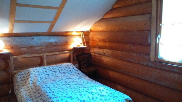 A cozy cabin room with a wooden bed, a small table, and a window. - Country Cottage / Gite - CHORGES (CHORGES)