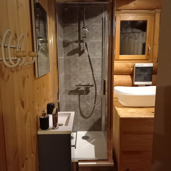 Un baño moderno con ducha envuelta en vidrio, un lavabo blanco y un mueble de tocador de madera.