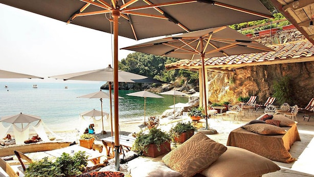 Een strandbar met buiten zitplaatsen en parasols, met uitzicht op zee.