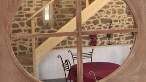 A circular window with a stone wall interior, wooden beams, and a table with chairs.