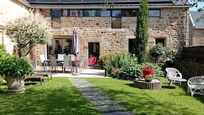 A stone house with a solar panel roof, a paved patio with outdoor furniture, and a well-maintained garden.