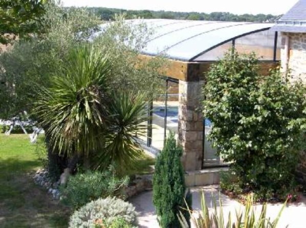 A greenhouse structure with a curved roof, surrounded by various plants and shrubs.