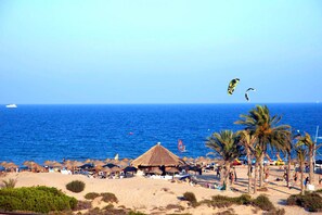 Una platja amb cabanes de teules, palmeres i un mar blau i transparent.