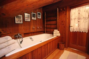 A wooden cabin bathroom with a bathtub, framed pictures on the wall, and a wooden door with lace curtains. - Apartment Pré Saint Didier for rent / 6 - 8 people (PRE' SAINT DIDIER)