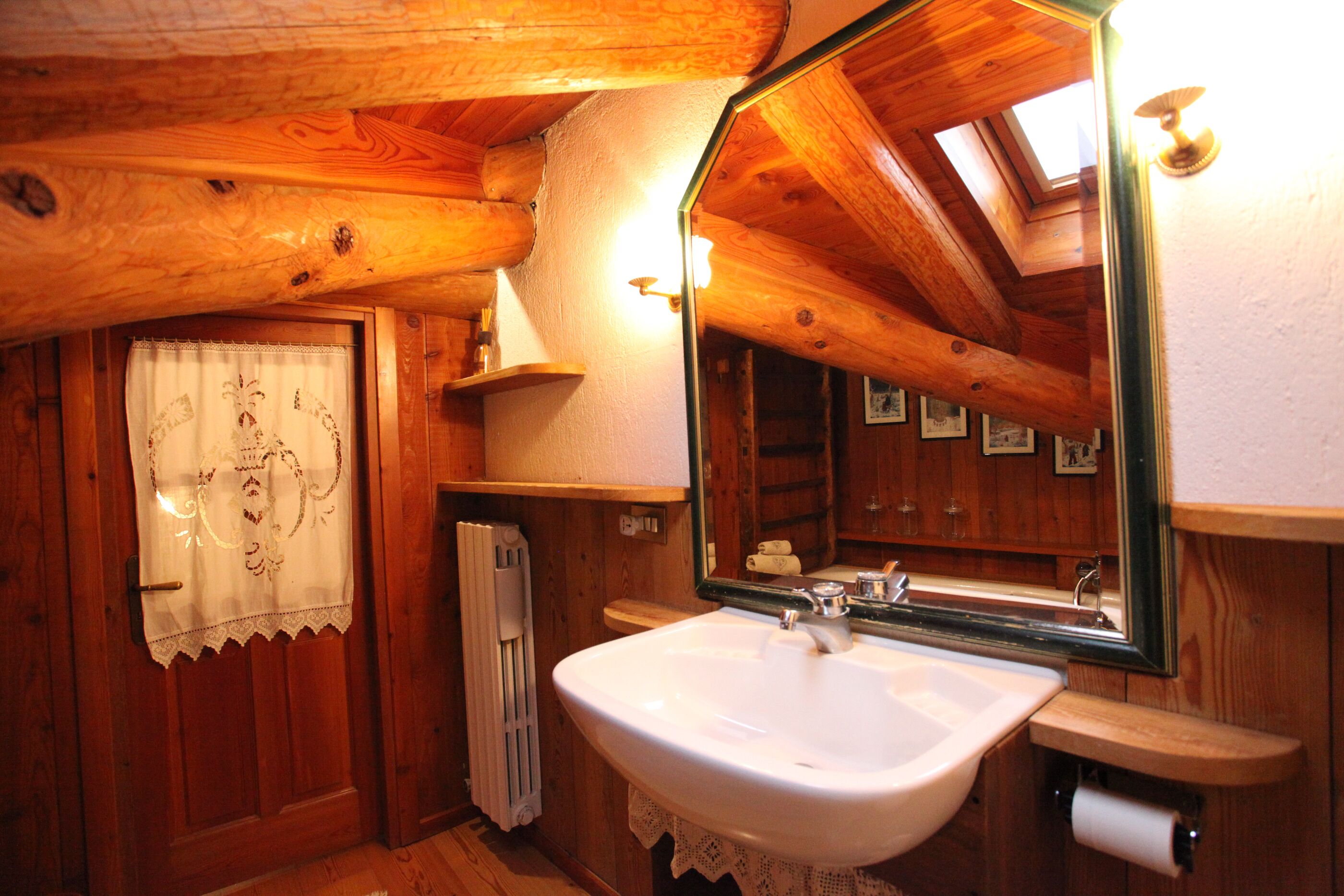 Un baño de cabaña de madera con un lavabo blanco, un espejo grande y un tragaluz.