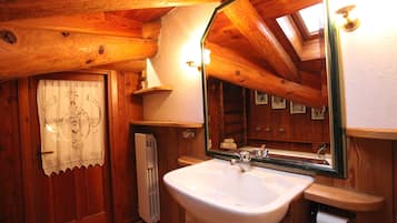 Un baño de cabaña de madera con un lavabo blanco, un espejo grande y un tragaluz.