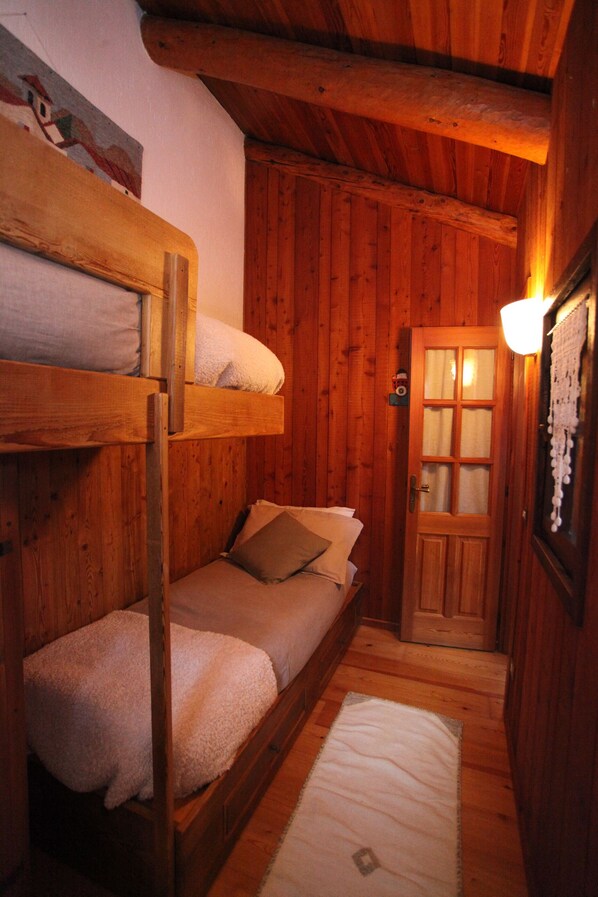 Une cabane en bois avec des lits superposés, une porte avec des panneaux de verre et un luminaire fixé au mur.