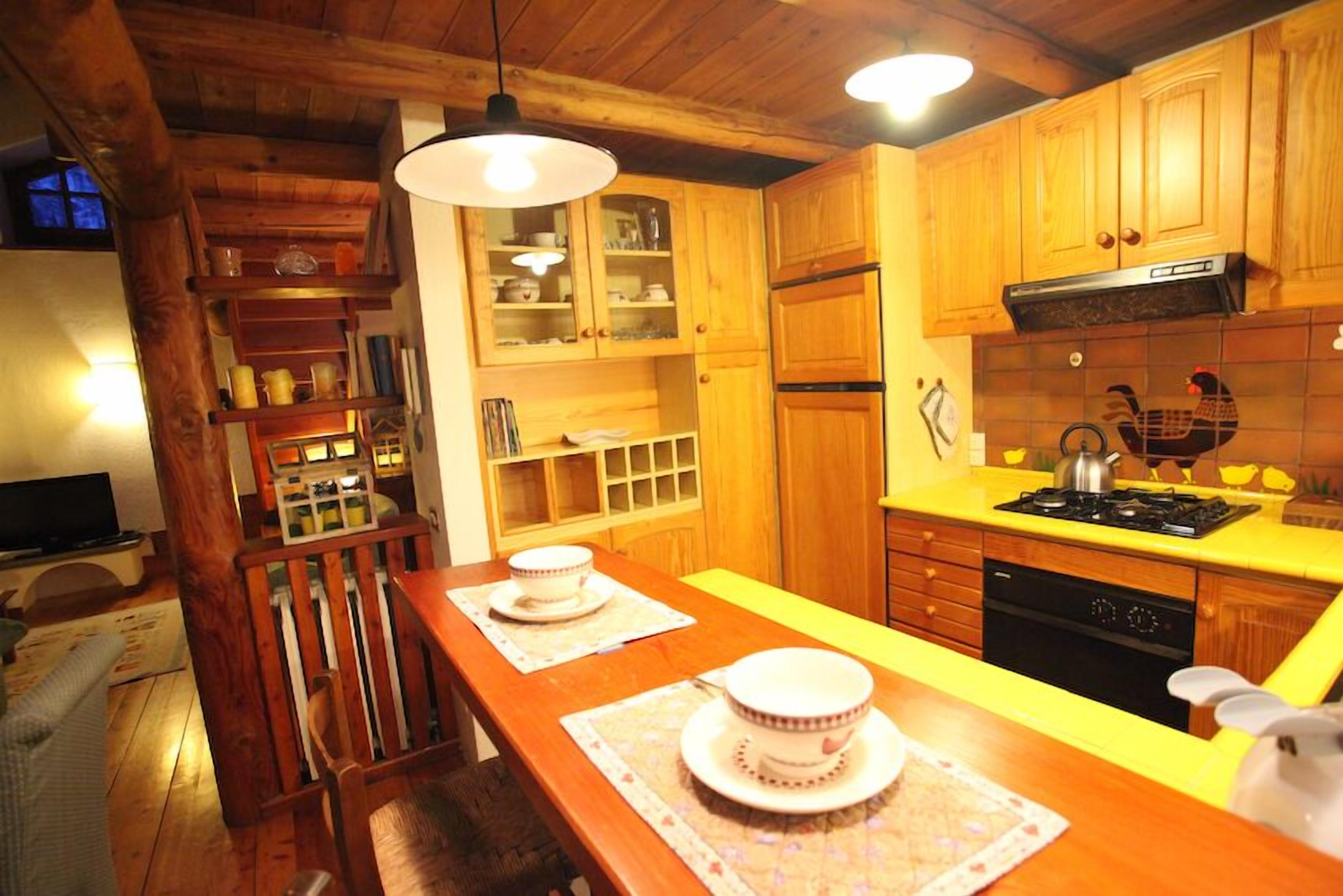 Une cuisine avec des meubles de rangement en bois, un plan de travail jaune, une cuisinière et une table à manger avec des tasses à thé.