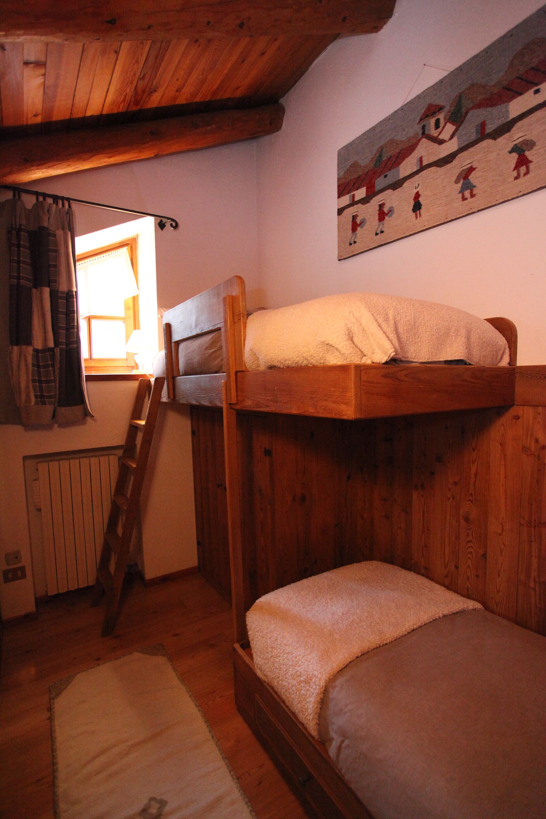 Un lit superposé en bois avec une échelle, une fenêtre avec des rideaux et un tableau accroché au mur.
