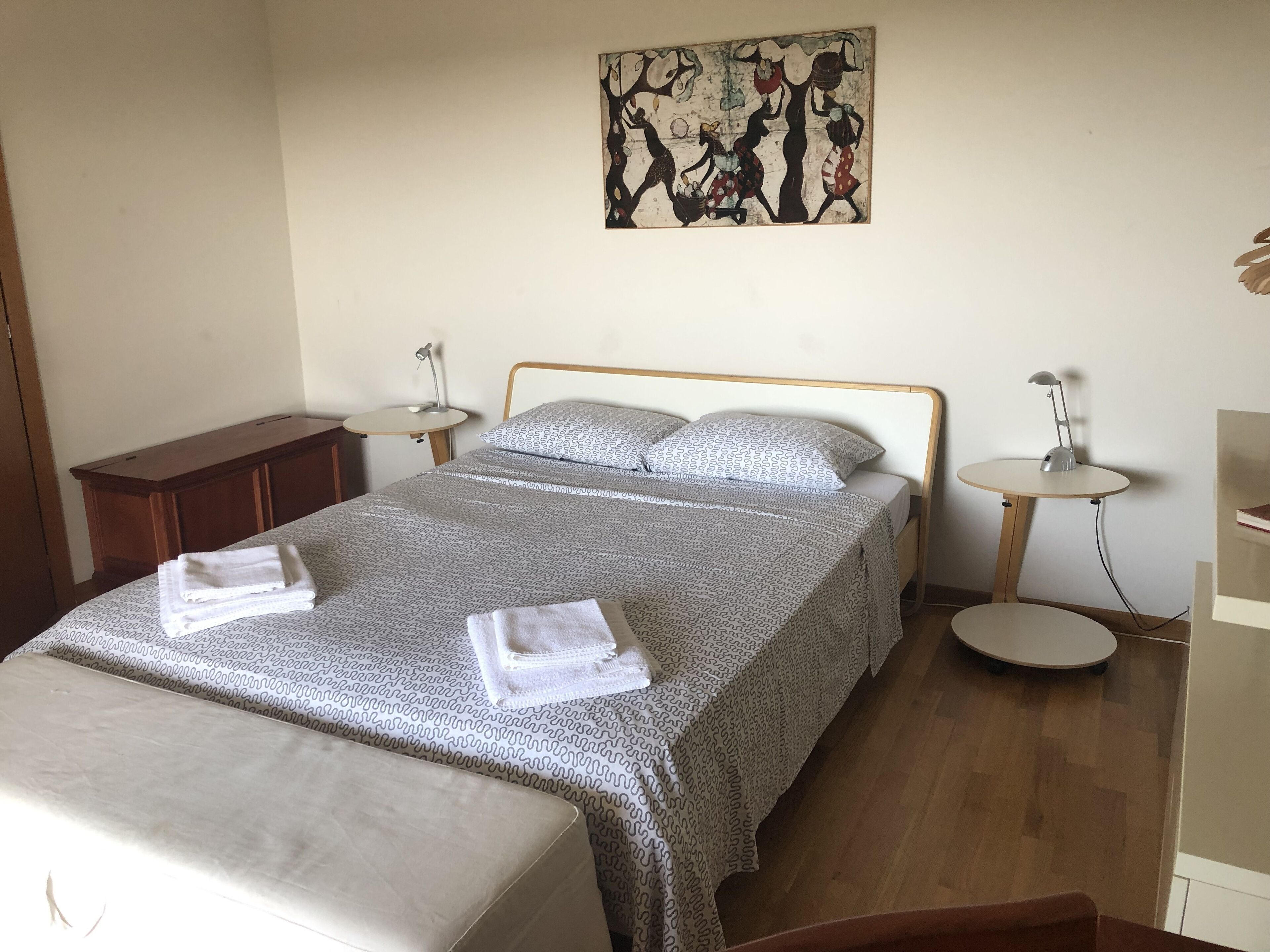 Un letto rifatto con lenzuola decorate, un comodino con una lampada e un'opera d'arte appesa al muro.